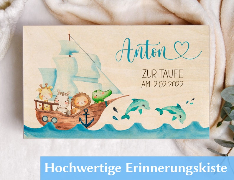 May include: A wooden keepsake box with a light wood background and a blue and green watercolor illustration of a ship with animals on it. The text "Anton Zur Taufe am 12.02.2022" is written on the box.