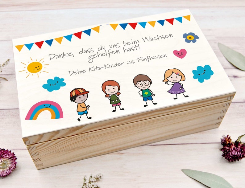 K&ouml;nnte beinhalten: Eine wei&szlig;e Holzkiste mit einem bunten handgezeichneten Design. Die Kiste hat einen Deckel mit einer Botschaft, die lautet: "Danke, dass du uns beim Wachsen geholfen hast! Deine Kita-Kinder aus F&uuml;nfhausen".