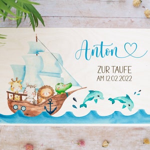 May include: A wooden sign with a blue and white sailboat with animals on it. The sign says "Anton Zur Taufe Am 12.02.2022" and has a blue heart.