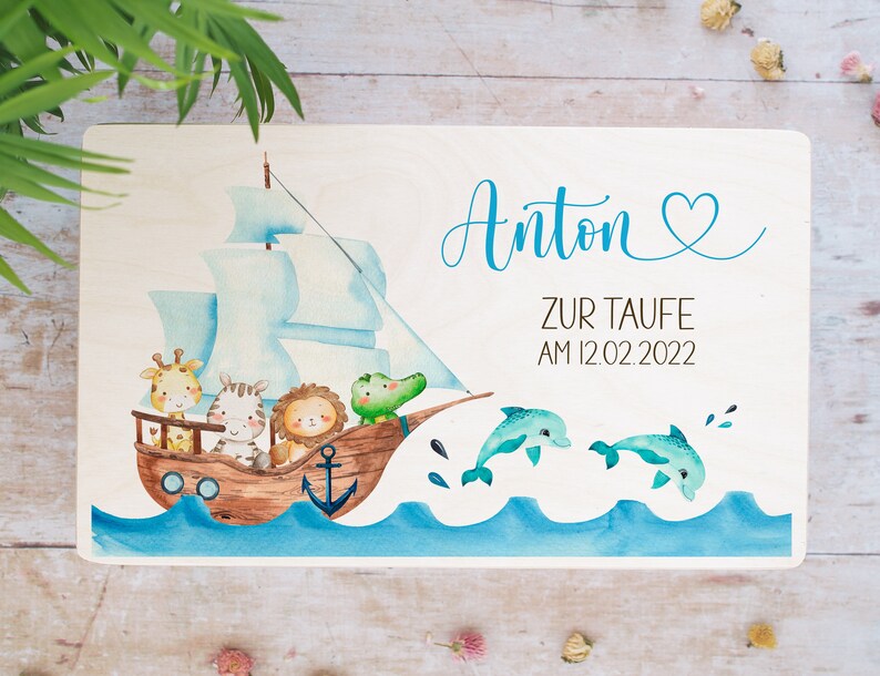 May include: A wooden sign with a blue and white sailboat with animals on it. The sign says "Anton Zur Taufe Am 12.02.2022" and has a blue heart.
