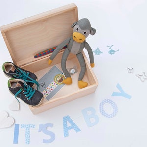 May include: A wooden box with a gray stuffed monkey toy inside. The box is open and there are baby shoes and a card that says "It's a boy!" on the inside. The box is surrounded by blue and white paper cutouts that spell out "It's a boy!"