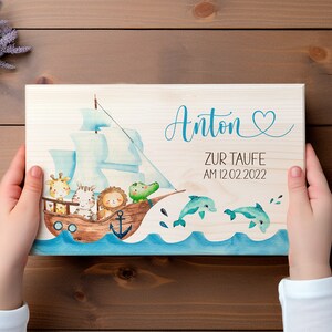 May include: A wooden sign with a blue and white sailboat, a giraffe, a zebra, a lion, and a crocodile. The sign says "Anton zur Taufe am 12.02.2022" and has a heart.