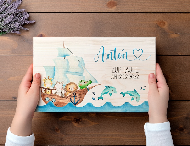 May include: A wooden sign with a blue and white sailboat, a giraffe, a zebra, a lion, and a crocodile. The sign says "Anton zur Taufe am 12.02.2022" and has a heart.