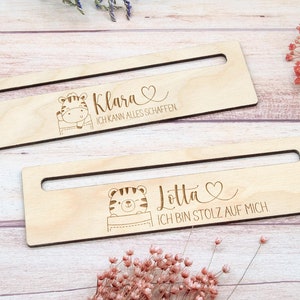 May include: Two wooden desk organizers with a rectangular shape and a cutout handle. Each organizer features a cartoon tiger illustration and personalized text: "Klara, I can do anything" and "Lotta, I am proud of myself."