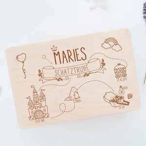 May include: A wooden treasure box with a personalized inscription "MARIES SCHATZTRUHE" and a whimsical illustration of a castle, a dinosaur, a carriage, and a treasure chest. The box is decorated with a crown, a rainbow, and stars.