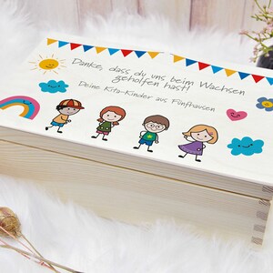 K&ouml;nnte beinhalten: Eine Holzkiste mit einem wei&szlig;en Deckel, der mit bunten Zeichnungen von Kindern, einem Regenbogen, einer Sonne und Wolken verziert ist. Der Deckel tr&auml;gt den Text "Danke, dass du uns beim Wachsen geholfen hast! Deine Kita-Kinder aus F&uuml;nfhausen".