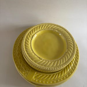Puede incluir: Una pila de platos de cer&aacute;mica amarillos. Los platos tienen un dise&ntilde;o texturizado y en relieve alrededor de los bordes. Los platos son de diferentes tama&ntilde;os, con un plato m&aacute;s peque&ntilde;o apilado encima de platos m&aacute;s grandes. Los platos son de color amarillo brillante.