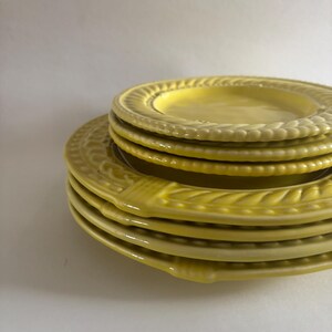 Puede incluir: Una pila de platos de cer&aacute;mica amarillos. Los platos tienen un borde decorativo en relieve. Los platos son de diferentes tama&ntilde;os, con un plato m&aacute;s peque&ntilde;o apilado encima de platos m&aacute;s grandes. Los platos son de color amarillo brillante.