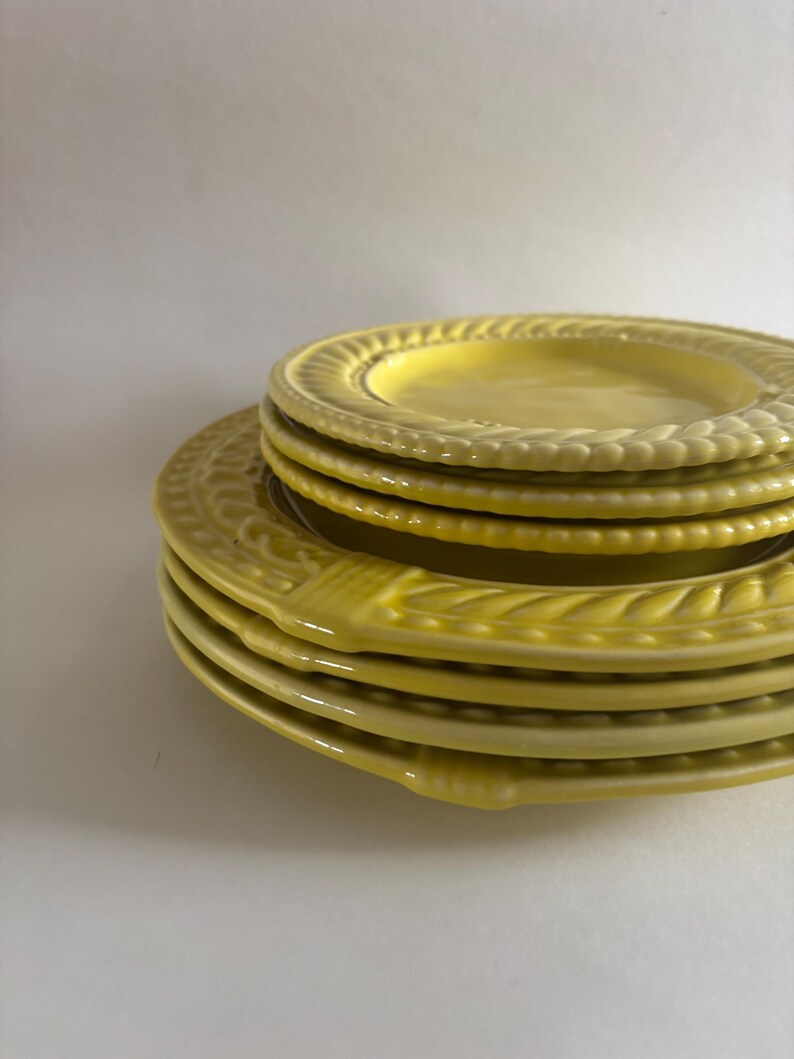 Puede incluir: Una pila de platos de cer&aacute;mica amarillos. Los platos tienen un borde decorativo en relieve. Los platos son de diferentes tama&ntilde;os, con un plato m&aacute;s peque&ntilde;o apilado encima de platos m&aacute;s grandes. Los platos son de color amarillo brillante.