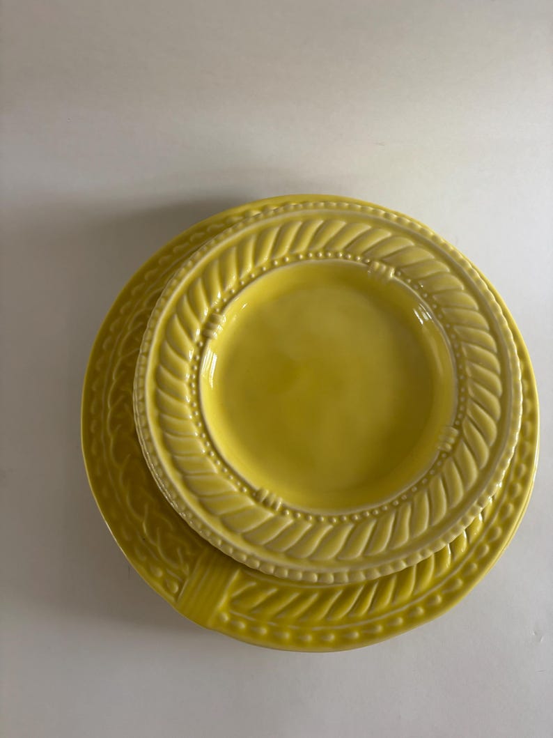 Puede incluir: Una pila de tres platos de cer&aacute;mica amarillos. El plato m&aacute;s grande tiene un borde decorativo en forma de cuerda. El plato del medio es m&aacute;s peque&ntilde;o y tiene un dise&ntilde;o similar. El plato m&aacute;s peque&ntilde;o es liso. Los platos son de un amarillo brillante.