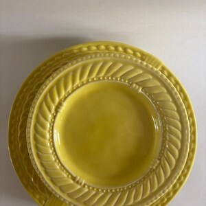 Puede incluir: Una pila de tres platos de cer&aacute;mica amarillos. Los platos tienen un dise&ntilde;o texturizado alrededor de los bordes, con un patr&oacute;n de hojas y peque&ntilde;os puntos. Los platos son de diferentes tama&ntilde;os, con el plato m&aacute;s peque&ntilde;o encima.