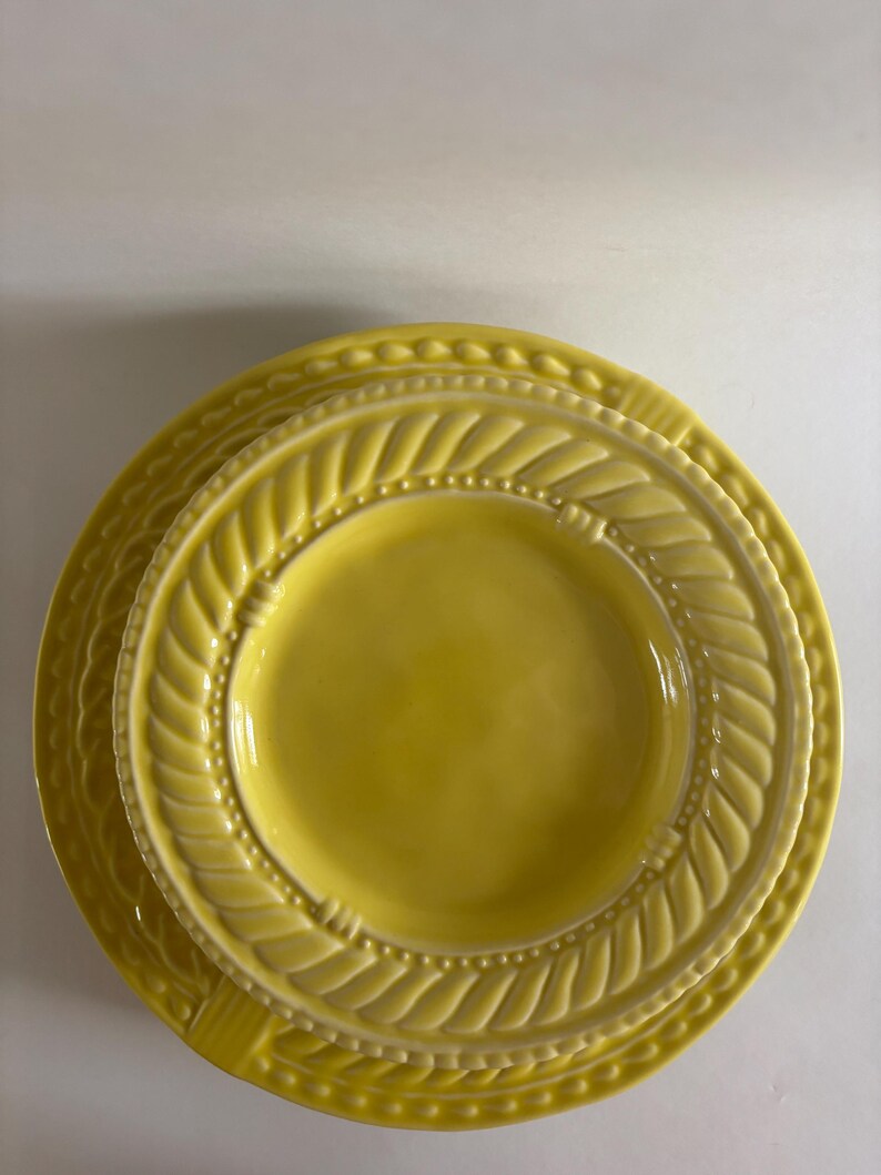 Puede incluir: Una pila de tres platos de cer&aacute;mica amarillos. Los platos tienen un dise&ntilde;o texturizado alrededor de los bordes, con un patr&oacute;n de hojas y peque&ntilde;os puntos. Los platos son de diferentes tama&ntilde;os, con el plato m&aacute;s peque&ntilde;o encima.