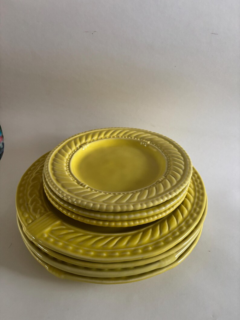 Puede incluir: Una pila de platos de cer&aacute;mica amarillos. Los platos tienen un borde decorativo en relieve con un patr&oacute;n de hojas y puntos. Los platos est&aacute;n apilados uno encima del otro, con el plato m&aacute;s peque&ntilde;o encima.