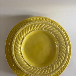 Puede incluir: Una pila de tres platos de cer&aacute;mica amarillos. Los platos tienen un borde decorativo en forma de cuerda y un borde con cuentas. Los platos est&aacute;n anidados, con el plato m&aacute;s peque&ntilde;o encima y el plato m&aacute;s grande debajo.