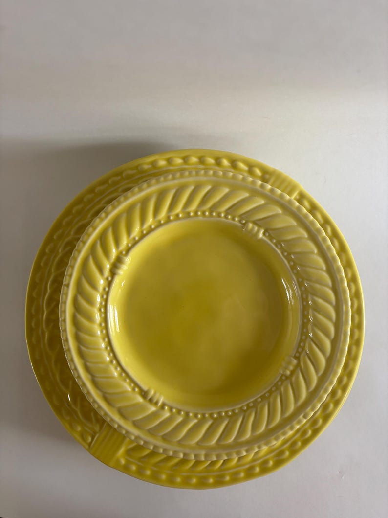 Puede incluir: Una pila de tres platos de cer&aacute;mica amarillos. Los platos tienen un borde decorativo en forma de cuerda y un borde con cuentas. Los platos est&aacute;n anidados, con el plato m&aacute;s peque&ntilde;o encima y el plato m&aacute;s grande debajo.