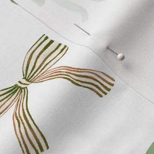 Pu&ograve; includere: Un tessuto bianco con un fiocco a strisce verdi e marroni. Il fiocco &egrave; annodato e le estremit&agrave; pendono. Ci sono due spilli nel tessuto.