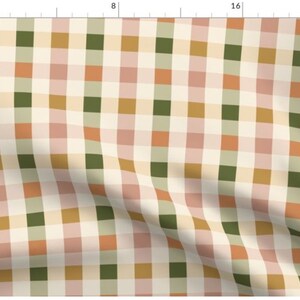 May include: A cream-colored fabric with a checkered pattern in shades of green, pink, orange, and gold. The fabric is folded in the bottom right corner.