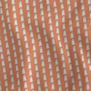 May include: A fabric featuring a repeating pattern of small white ghosts with dark eyes on a solid terracotta orange background. The ghosts are arranged in a grid-like formation across the textile, creating a consistent and uniform visual design.