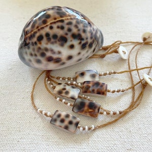 May include: A set of five brown and white shell bracelets with brown string and white beads. The bracelets are tied together with a larger brown and white shell.
