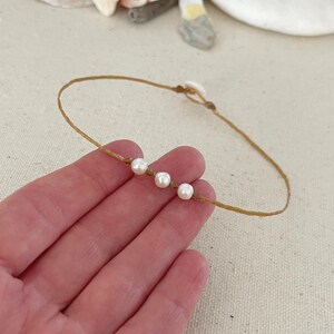 May include: A simple necklace made with brown string and four white pearls.