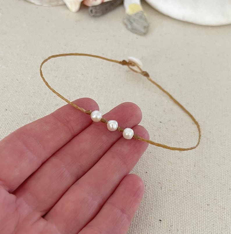 May include: A simple necklace made with brown string and four white pearls.