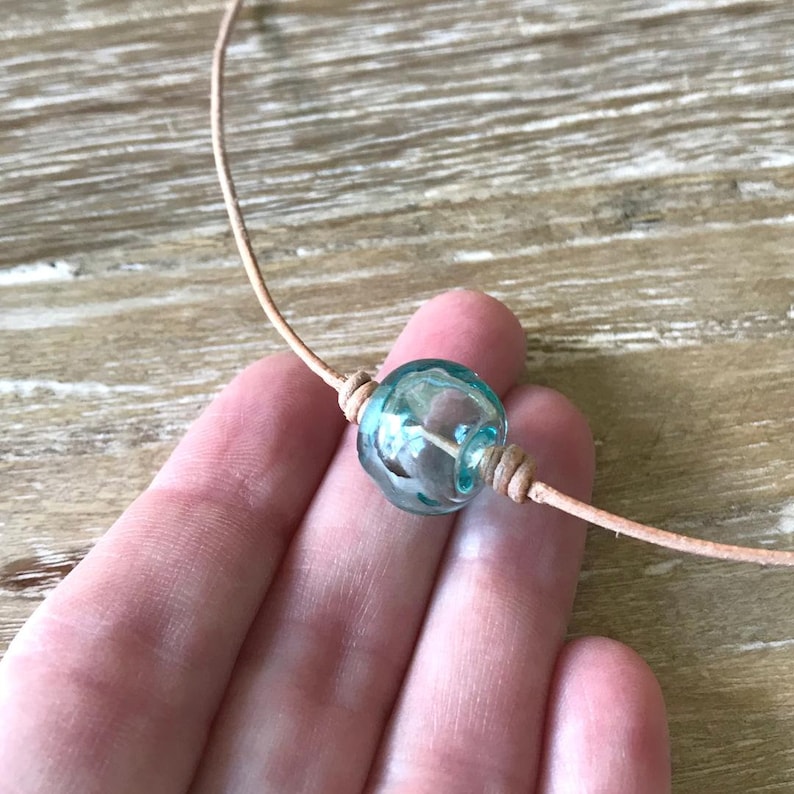 May include: A light blue glass bead necklace with a brown leather cord.