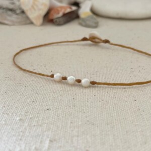 May include: A simple brown string bracelet with four white pearls.