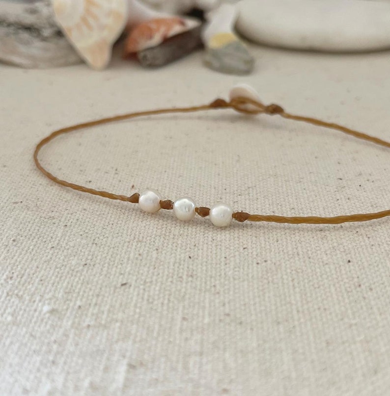 May include: A simple brown string bracelet with four white pearls.