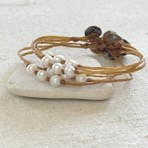 May include: A brown leather bracelet with multiple strands and a cluster of white pearls.