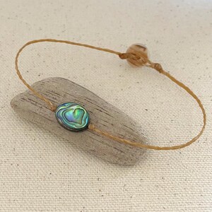 May include: A brown cord bracelet with a green, blue, and iridescent abalone shell charm.