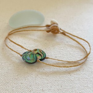 Op de afbeelding: Een eenvoudige ketting met twee iriserende abalone-schelp kralen op een bruin koord.