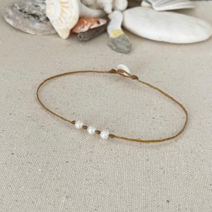 May include: A simple brown string bracelet with four white pearl beads.