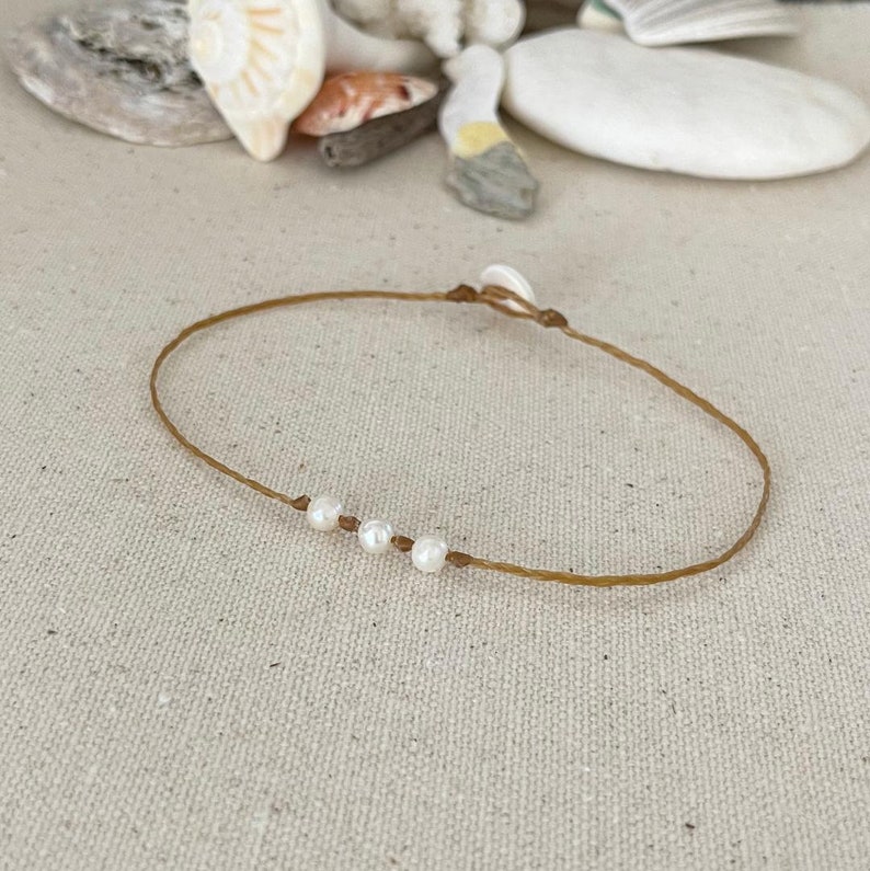 May include: A simple brown string bracelet with four white pearl beads.