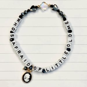 Peut inclure: Un bracelet de perles avec les mots "WHO'S AFRAID OF LITTLE ME" épelés en perles de lettres blanches. Le bracelet comporte des perles noires, un charme de camée et une perle irisée transparente.