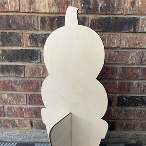 May include: Unpainted wooden cutout of an ice cream cone with three scoops of ice cream. The cone is standing upright on a checkered surface.