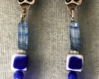 May include: A pair of silver dangle earrings with blue and white glass beads. The top of the earrings feature a silver flower design.