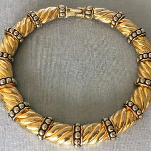 May include: A gold-toned necklace with a twisted rope design. The necklace features alternating sections of twisted gold metal and silver-toned accents with small, round details. The clasp is gold-toned.