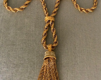 May include: A gold-tone necklace with a twisted rope chain and a tassel pendant. The tassel is made of multiple strands of chain and has a small, round, rhinestone-encrusted top.