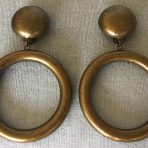 May include: A pair of gold-toned clip-on earrings with large round hoops. The hoops are thick and have a smooth, polished finish.