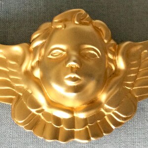 May include: A gold cherub figurine with wings, the cherub has a sweet expression on its face.
