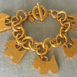 Op de afbeelding: Een gouden armband met een kettinglink-ontwerp en meerdere hangende bedels in de vorm van kleine honden.