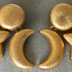 May include: Gold tone earrings with a star, crescent moon, and circle design.