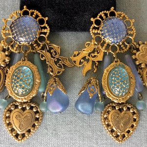 May include: Gold tone dangle earrings with blue and green glass beads and charms. The earrings feature a large blue glass center piece with a filigree design.