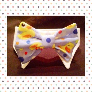 Puede incluir: Una pajarita azul con cuello blanco, con un patrón de patitos de goma amarillos y lunares de colores.