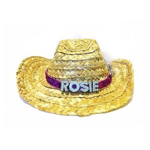 以下が含まれることがあります： ピンクのグリッターバンドと「ROSIE」と書かれたシルバーのネームプレートが付いた麦わら製のカウボーイハットです。