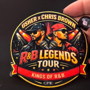 Könnte beinhalten: Ein runder bestickter Aufnäher mit Porträts von Usher und Chris Brown mit Sonnenbrillen, beschriftet mit USHER X CHRIS BROWN, R&B LEGENDS TOUR und KINGS OF R&B. Das Design zeigt zwei Mikrofone, rote Scheinwerfer und ein rotes Banner auf schwarzem Hintergrund.