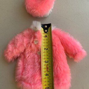 May include: A pink faux fur coat with a white trim and a matching pink faux fur hat. The coat is 5 inches long and the hat is 2.5 inches in diameter.