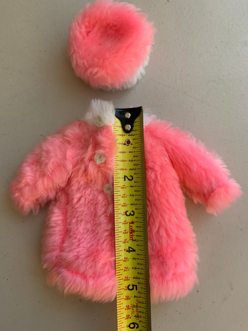 May include: A pink faux fur coat with a white trim and a matching pink faux fur hat. The coat is 5 inches long and the hat is 2.5 inches in diameter.