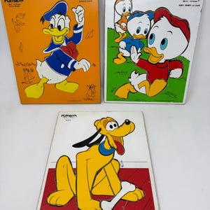 May include: Three vintage Playskool wooden puzzles featuring Disney characters. One puzzle shows Donald Duck on an orange background. Another depicts Huey, Dewey, and Louie on a green background. The third puzzle features Pluto.
