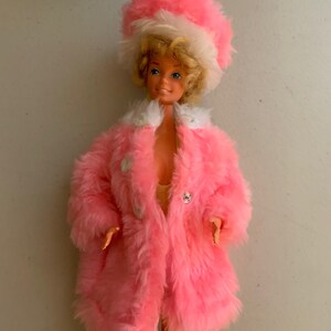 May include: A vintage Barbie doll wearing a pink fur coat and a white and pink fur hat. The doll has blonde hair and blue eyes.